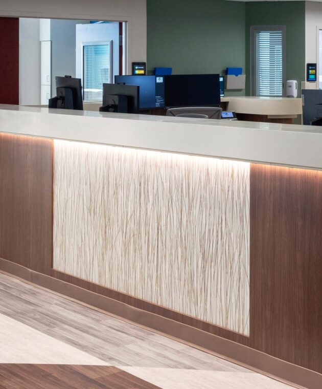Close up on a nurse's station counter. The counter has a walnut woodgrain and a horizontally centered rectangular panel of resin material features encapsulated long blades of glass.