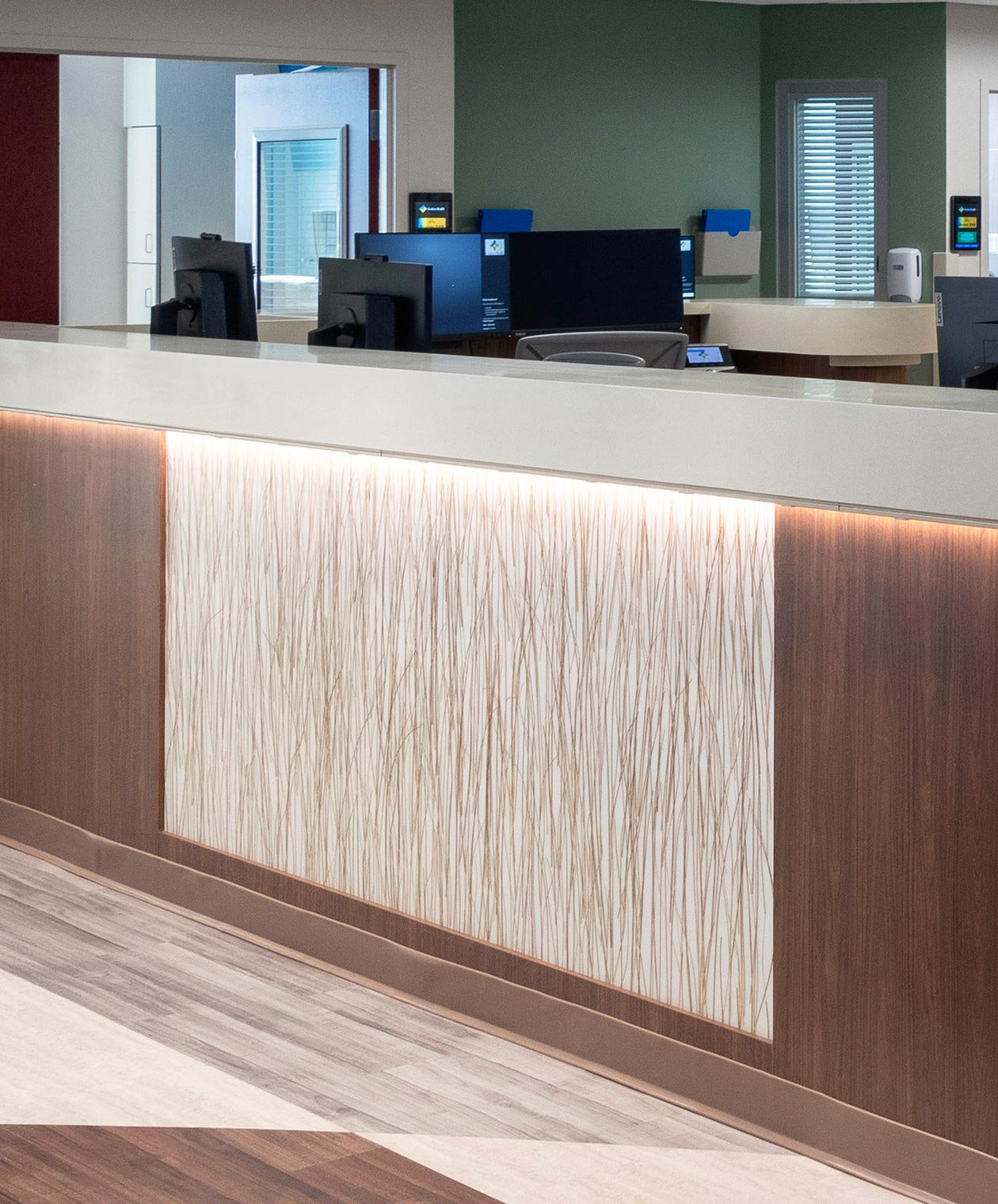Close up on a nurse's station counter. The counter has a walnut woodgrain and a horizontally centered rectangular panel of resin material features encapsulated long blades of glass.